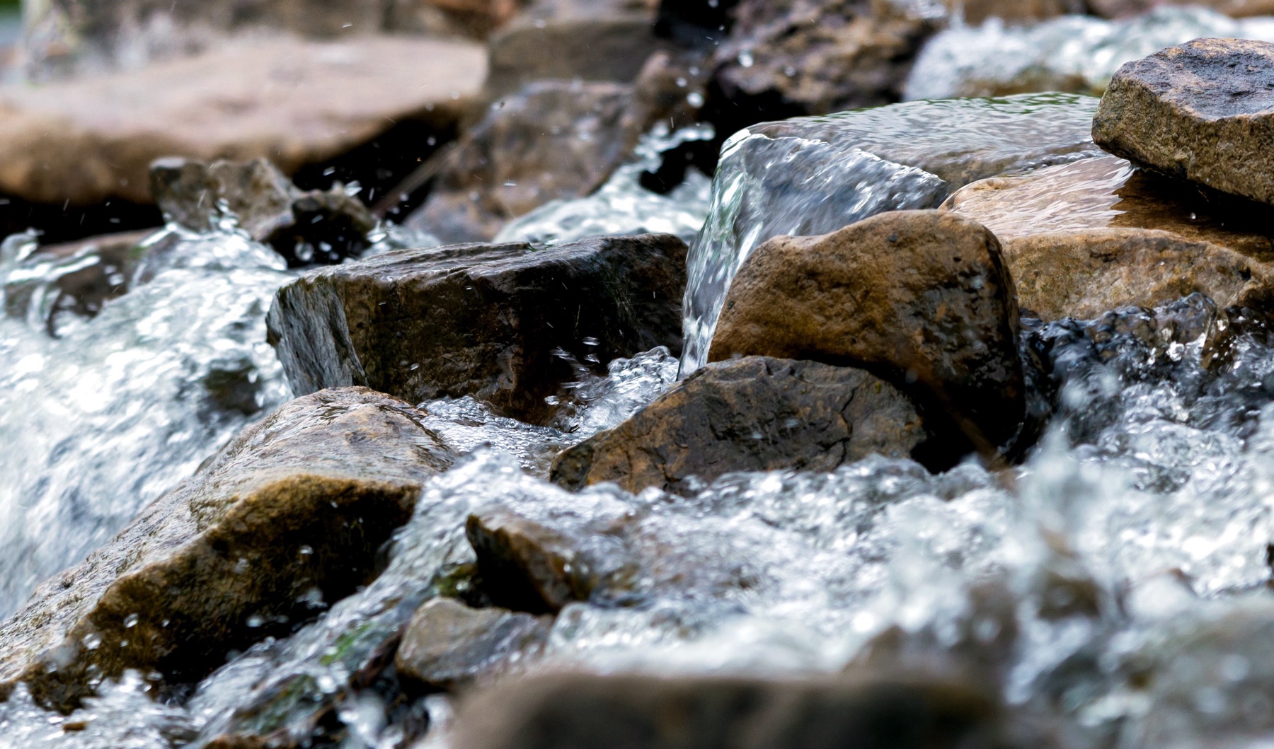 Clear water rushing over smooth stones in a stream.